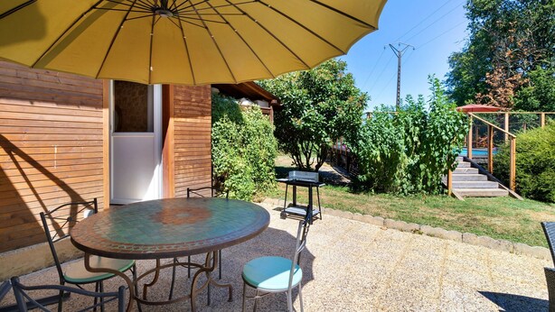 An outdoor patio with a round table and chairs, a yellow umbrella, and a wooden building with a door. - Apartment 'La Clésinerie' with Private Pool, Private Terrace and Wi-Fi (Badefols-sur-Dordogne)
