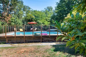 Ein Garten mit Swimmingpool, einer überdachten Sitzgelegenheit und einer umzäunten Terrasse.