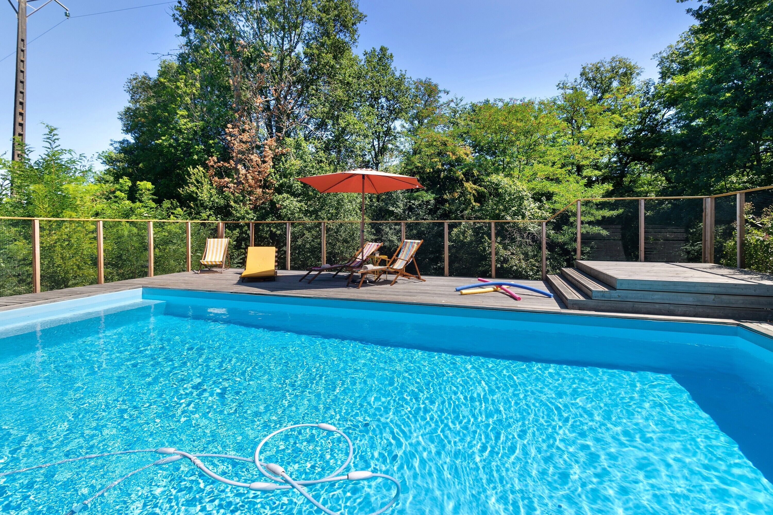 Une piscine à l’eau d’un bleu cristallin, entourée d’une terrasse en bois et de chaises longues.