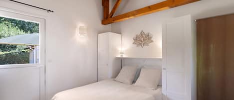 A bedroom with a bed, a window, a wall-mounted light, and a door.