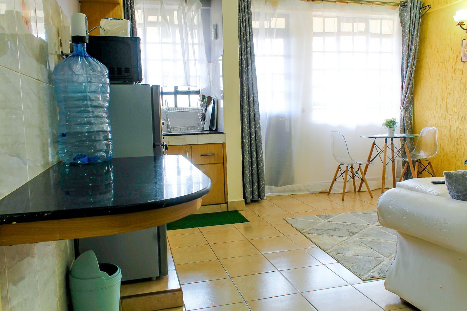 Cocina con dispensador de agua, microondas y lavabo. Hay un comedor con una silla y una mesa.