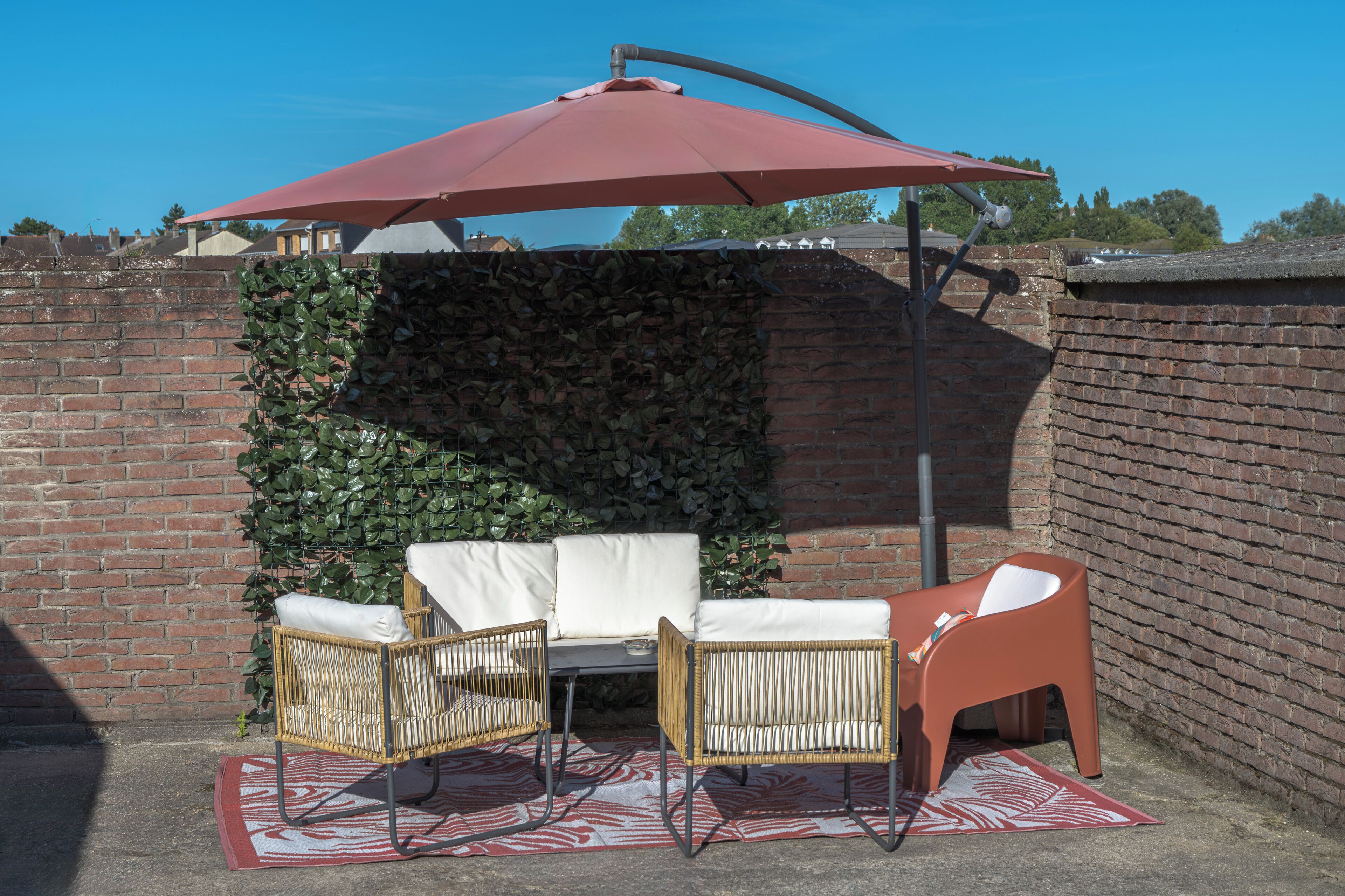Ein Patio mit Backsteinmauer, rotem Sonnenschirm und Korbmöbeln.