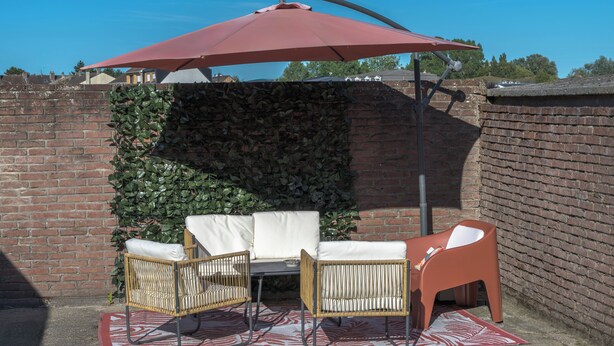 En patio med murstensvæg, rød parasol og fletmøbler.