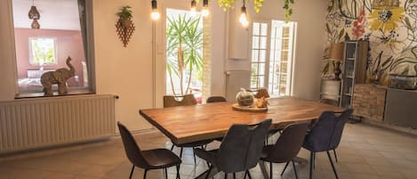 A dining area with a wooden table, six chairs, hanging light bulbs, and a view of a room with a window and a radiator.