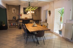 Uma área de refeições com mesa de madeira, cadeiras, parede de tijolos e plantas penduradas.