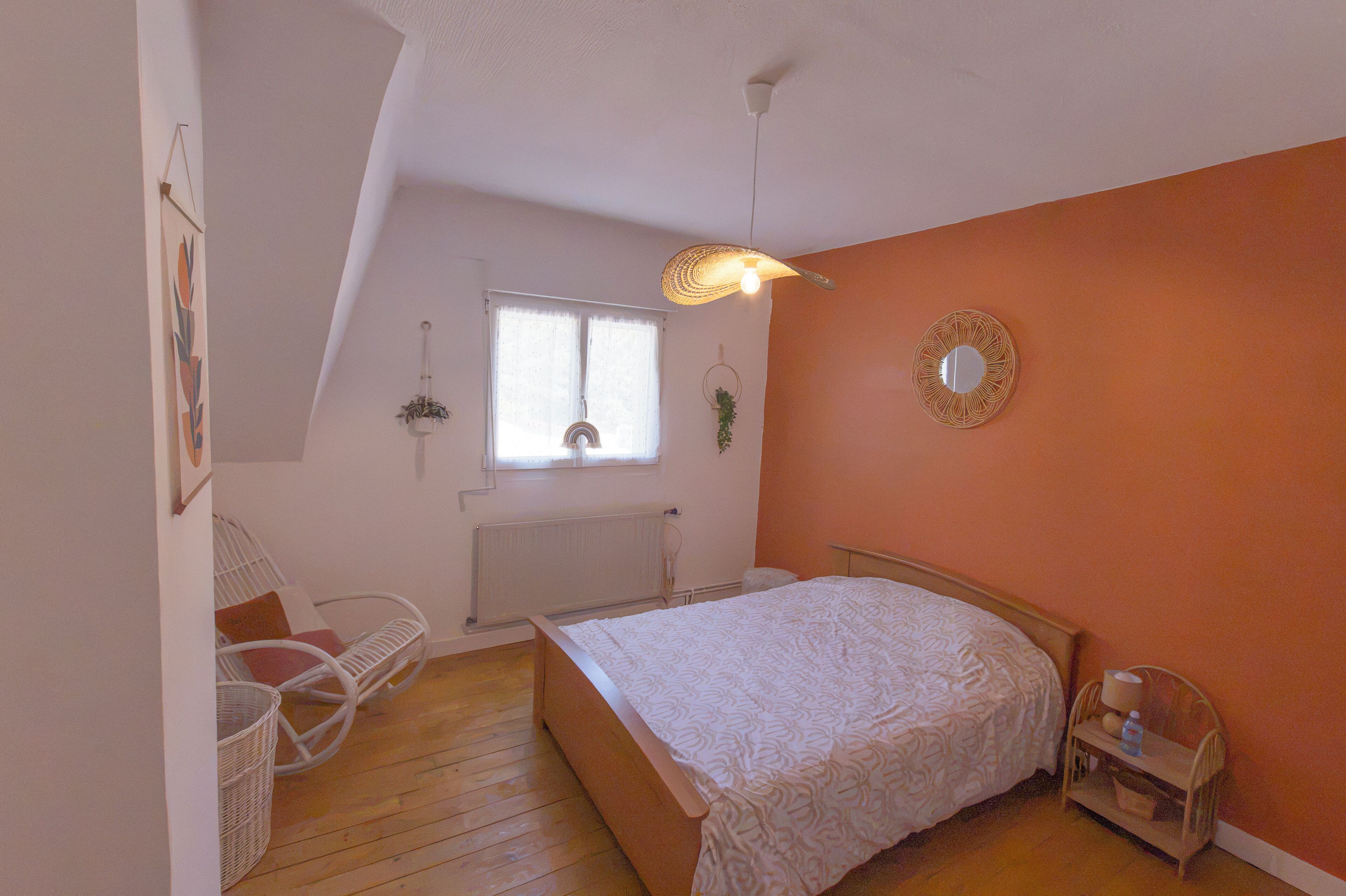 Un dormitorio con cama, una silla, una mesita, un radiador y una ventana con cortinas.