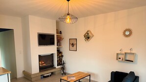 A living room with a fireplace, a TV, a sofa, a coffee table, and a hanging light fixture.