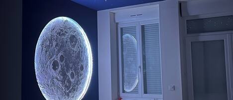 Un dormitorio con un mural grande e iluminado de la luna, una ventana con persianas y un radiador.