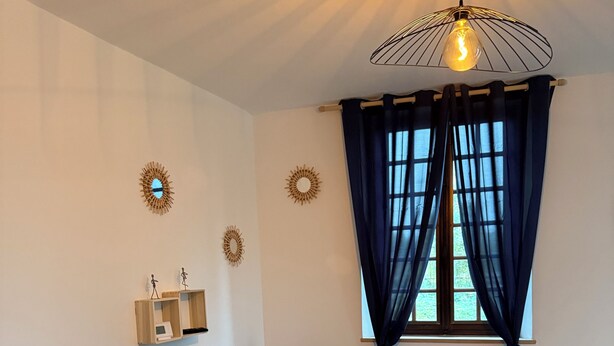 A modern living room with a black sofa, a wooden coffee table, a hanging light fixture, and decorative wall mirrors.