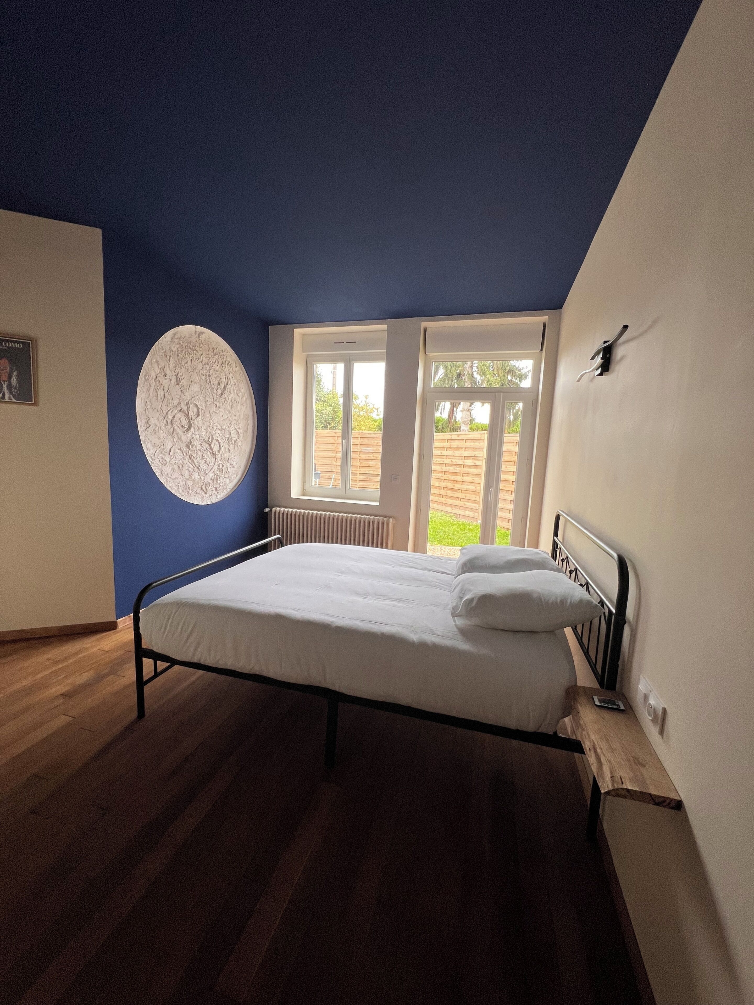 Un dormitorio con una cama, un adorno circular en la pared y una ventana con vistas a la vegetación.