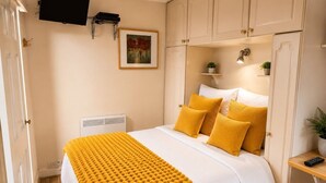 A bedroom with a bed, a television mounted on the wall, and a painting above the bed.