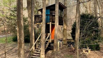 A treehouse with a wooden staircase leading up to a platform with a railing.