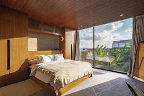 Un dormitorio con cabecera de madera, una cama grande, una ventana con cortinas y vistas a la vegetación exterior.