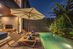 Un área junto a la piscina con sillones de descanso, una sombrilla y un televisor.