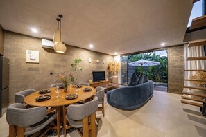 Un área de comedor moderna con una mesa redonda, sillas grises, un sofá azul y un televisor.
