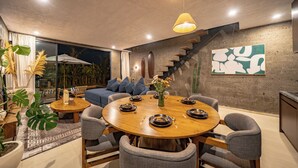 Un espace repas moderne avec une table ronde en bois, des chaises à revêtement gris et un escalier menant à un niveau supérieur.