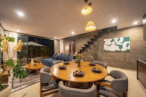 Un comedor moderno con una mesa redonda de madera, sillas tapizadas grises y una escalera que sube a un nivel superior.