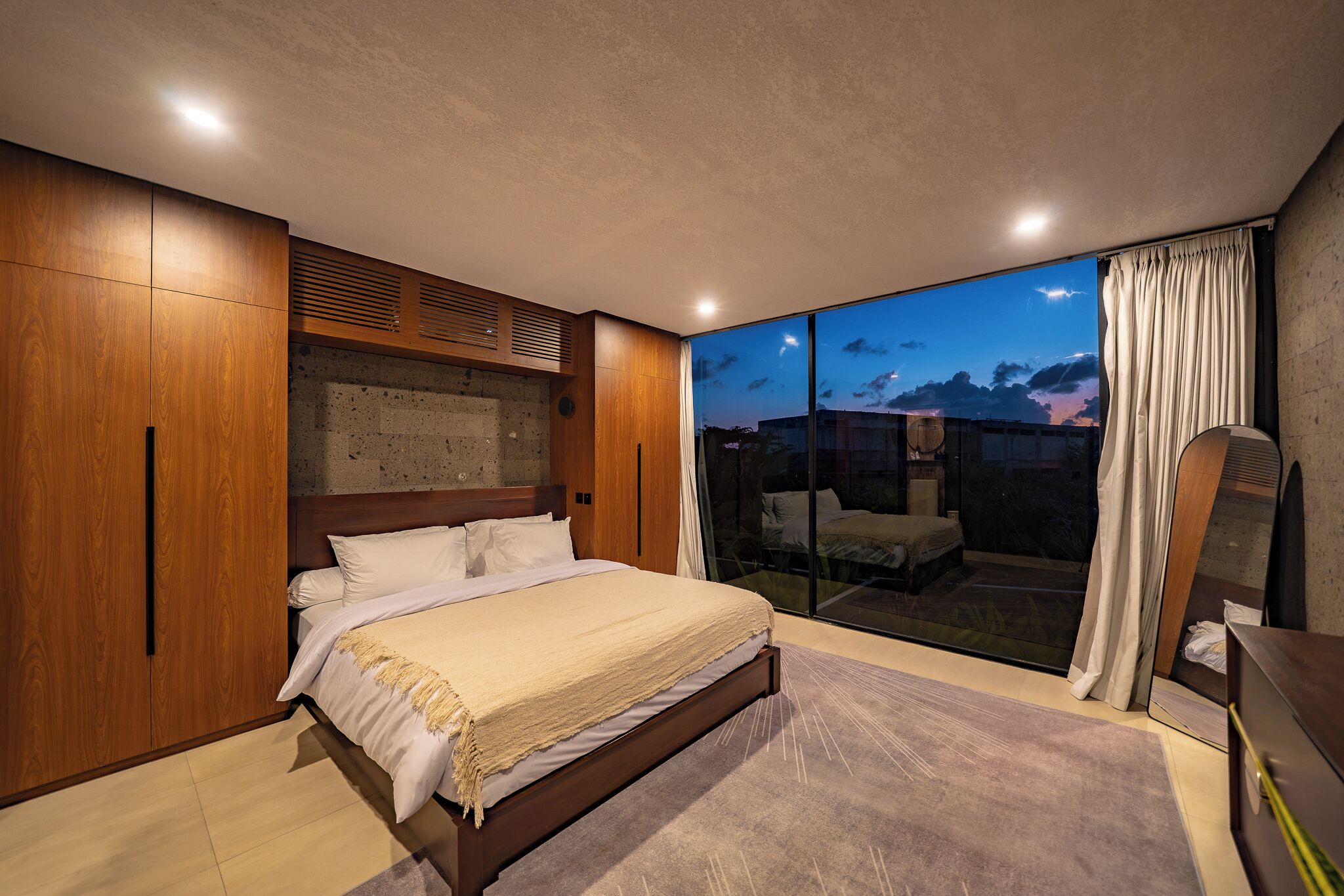 A bedroom with a large bed, wooden wardrobe, and a sliding glass door leading to a balcony.