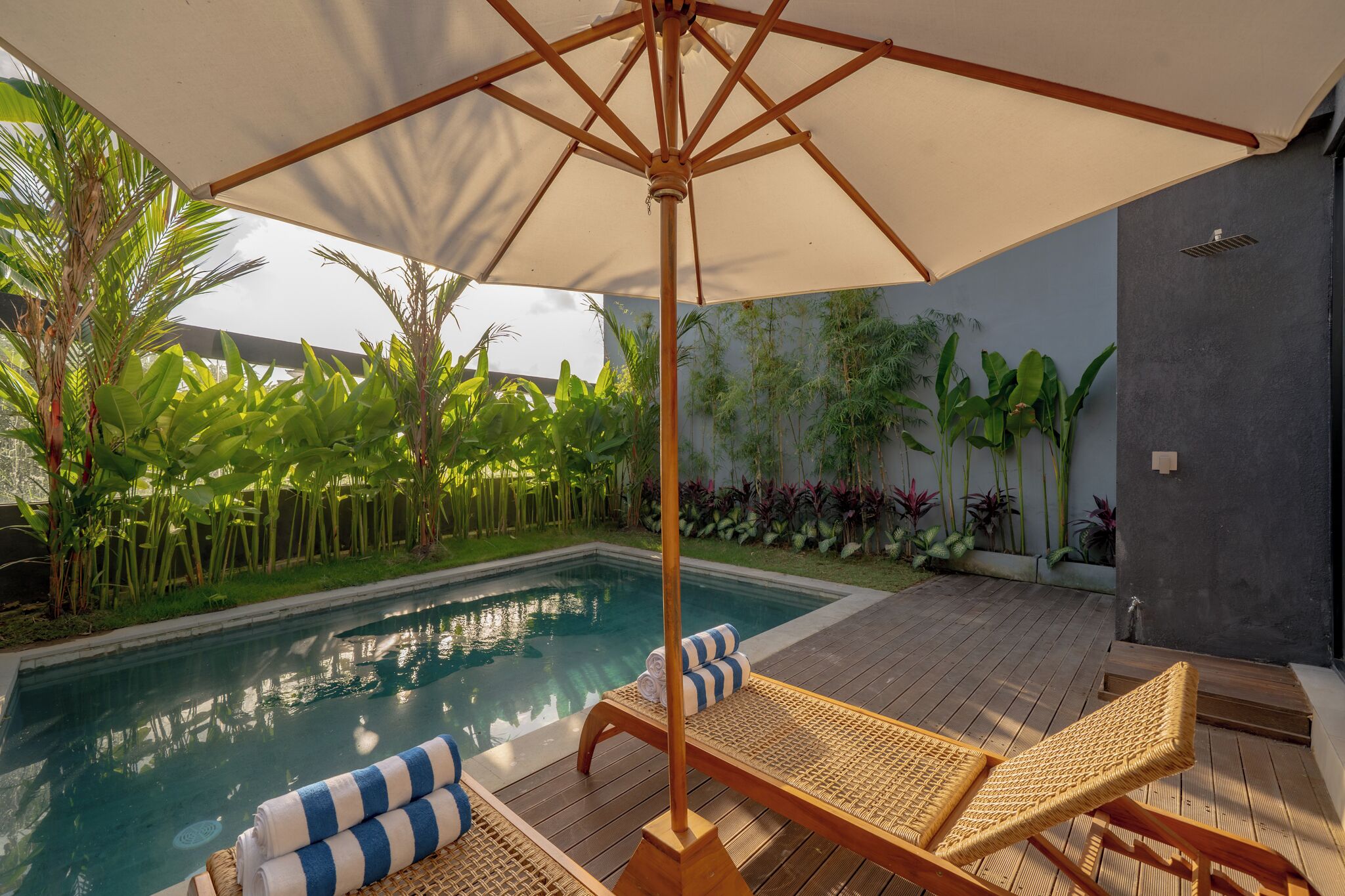 A poolside area with a wooden deck, lounge chairs, and an umbrella.