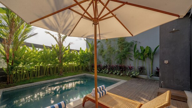 Un espace aménagé au bord de la piscine, avec une terrasse en bois, des chaises longues et un parasol.
