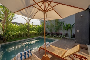 A poolside area with a wooden deck, lounge chairs, and an umbrella. - Lara Residence 1 Canggu (Canggu)
