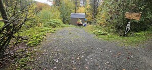 A gravel path leading to a small building with a metal roof, surrounded by dense foliage and a wooden sign.