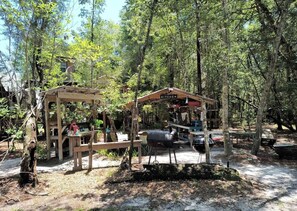 A rustic outdoor kitchen area with a wooden structure, a barbecue grill, and a dining table. - Off-Grid Nature Retreat Near Satilla River, Georgia (WAYNESVILLE)