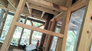 A wooden interior with a sloped ceiling and exposed beams, large windows, and a visible outdoor area.