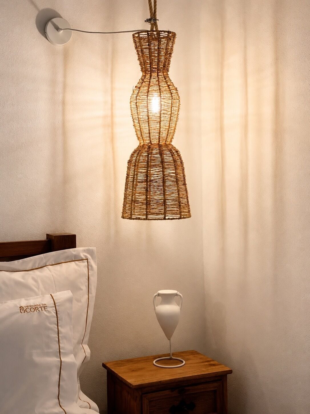 Una habitació amb un llit, una taula de nit amb una làmpada i una làmpada penjant.