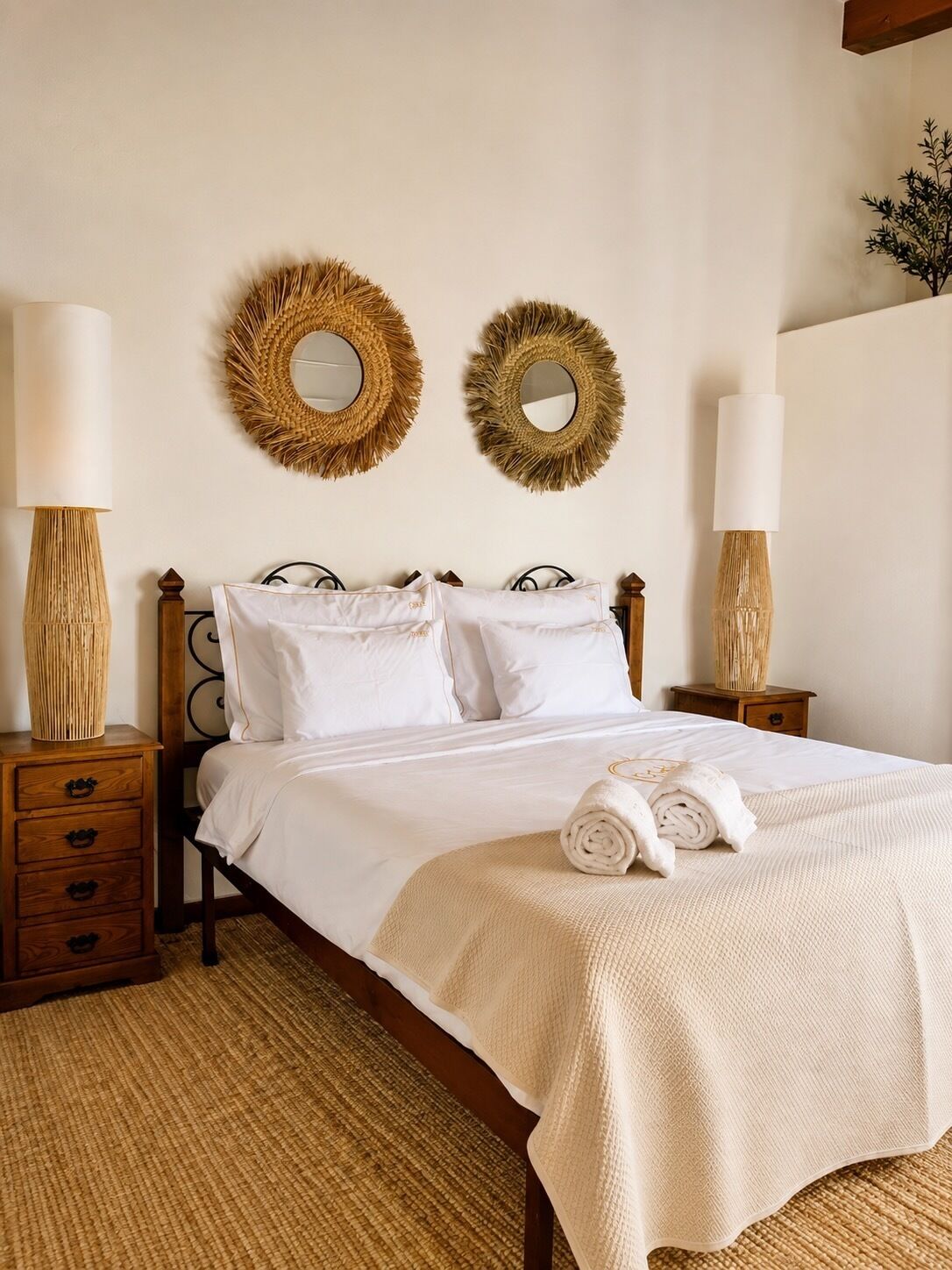 A neatly made bed with white linens, two wall-mounted mirrors, and a bedside lamp on a wooden nightstand.