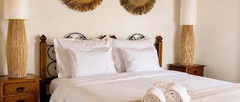 Een net opgemaakt bed met witte lakens, twee spiegels aan de muur en een bedlamp op een houten nachtkastje.