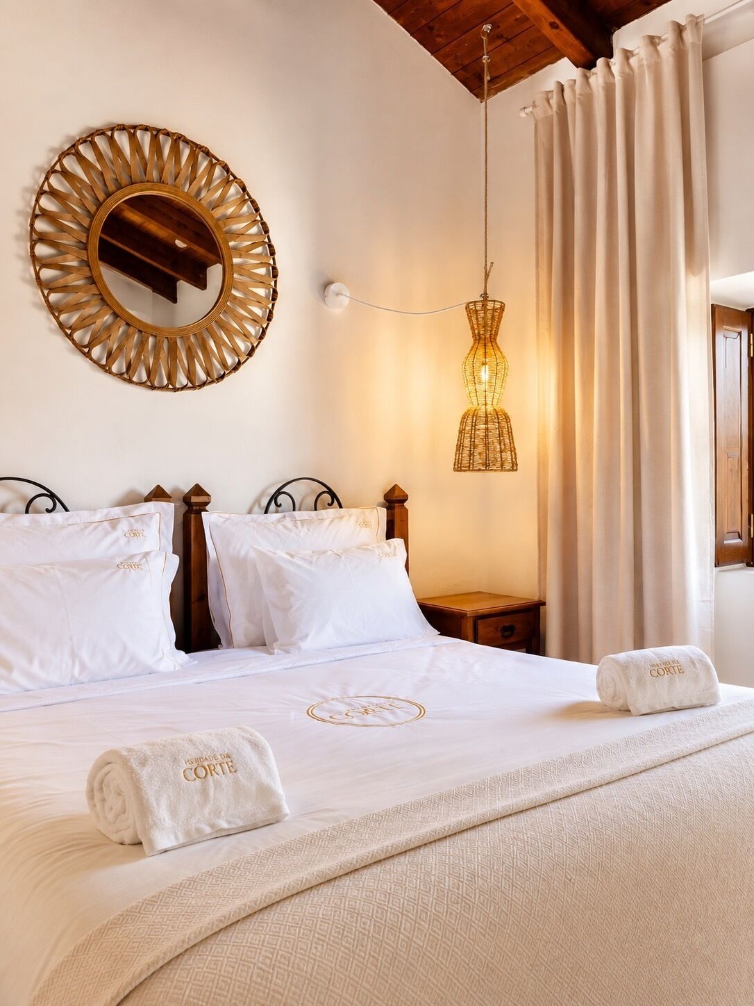 Une chambre d’hôtel avec un lit, un miroir rond, un luminaire suspendu et une fenêtre avec des rideaux.