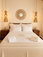 Habitación de hotel con una cama grande, dos mesitas de noche, un espejo redondo y dos lámparas de pared.