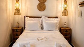 A hotel room with a bed, two bedside tables, a wall-mounted light fixture, and a decorative wall hanging.