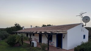 A white building with a tiled roof, a satellite dish, and a covered patio area with chairs.