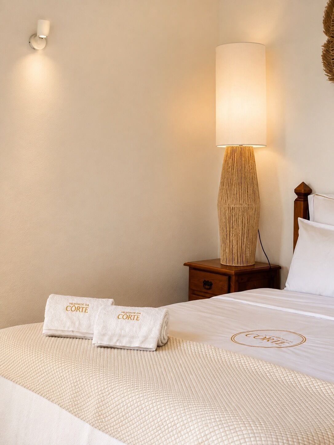 A hotel room with a neatly made bed, a bedside lamp, and a towel with branding.