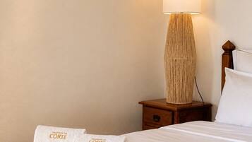 A hotel room with a neatly made bed, a bedside lamp, and a towel with branding.