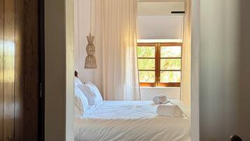 A bedroom with a wooden ceiling, a bed with white bedding, a window with curtains, and a hanging light fixture.