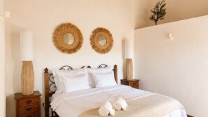 A bedroom with a wooden bed frame, two bedside tables with lamps, a wall-mounted mirror, and a small plant.