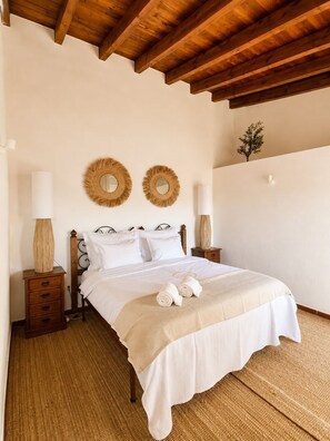 A bedroom with a wooden bed frame, two bedside tables with lamps, a wall-mounted mirror, and a small plant.