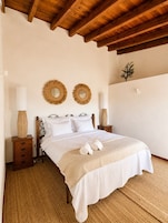 A bedroom with a wooden bed frame, two bedside tables with lamps, a wall-mounted mirror, and a small plant.