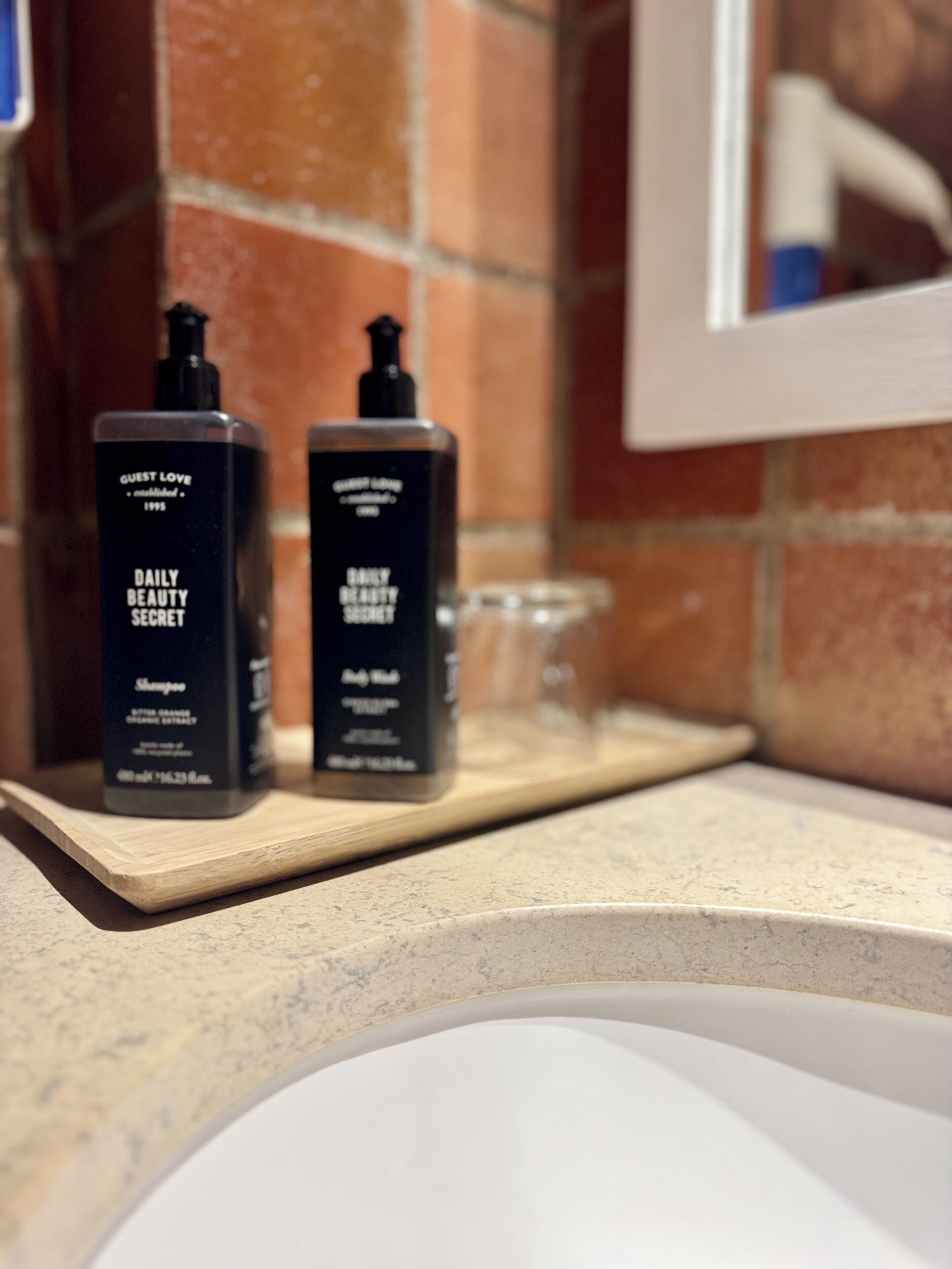 Deux bouteilles noires sur une étagère en bois, avec un lavabo de salle de bain au premier plan.