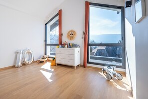 A bright room with wooden flooring, a white dresser, a child's chair, and a toy car near a large window with a view of buildings. - Stunning Villa in Menton, (Menthon saint bernard)