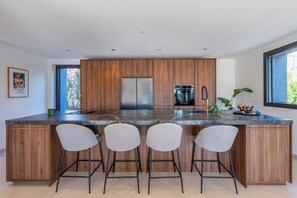 A modern kitchen with a central island, bar stools, stainless steel appliances, and a view through the window. - Stunning Villa in Menton, (Menthon saint bernard)