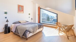 Un dormitori amb un llit, una cadira, una finestra i una làmpada.