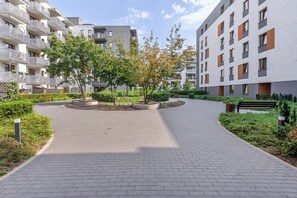 Ein gepflasterter Weg in einer Wohnanlage mit modernen Gebäuden, einer runden Gartenanlage und einer Bank.