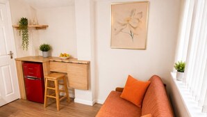 A compact living space with a kitchenette, a sofa with cushions, and a painting on the wall. - Suite in LS7, Great For Contractors (West Yorkshire)