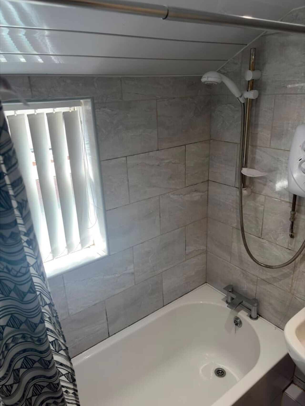 A bathroom with a shower, a window, and a sink.