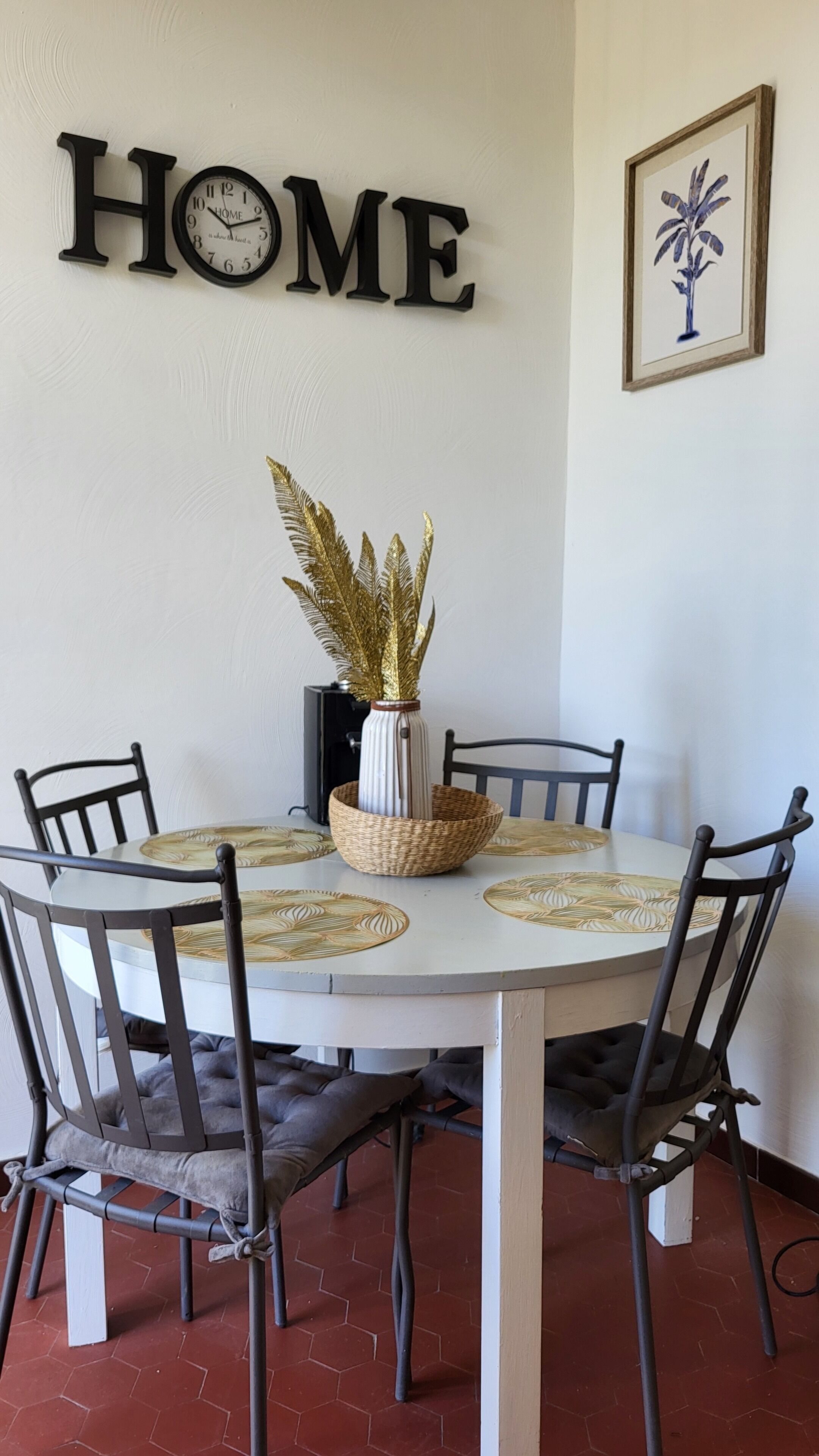 A dining table with a white top, surrounded by black chairs, and a decorative vase with golden leaves.