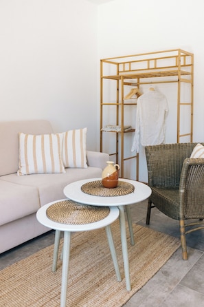 A minimalist living space with a sofa, two round tables, a wicker chair, a wooden shelf unit, and a woven rug. - Appartamento Wood - Tenuta Fascianello (Puglia)